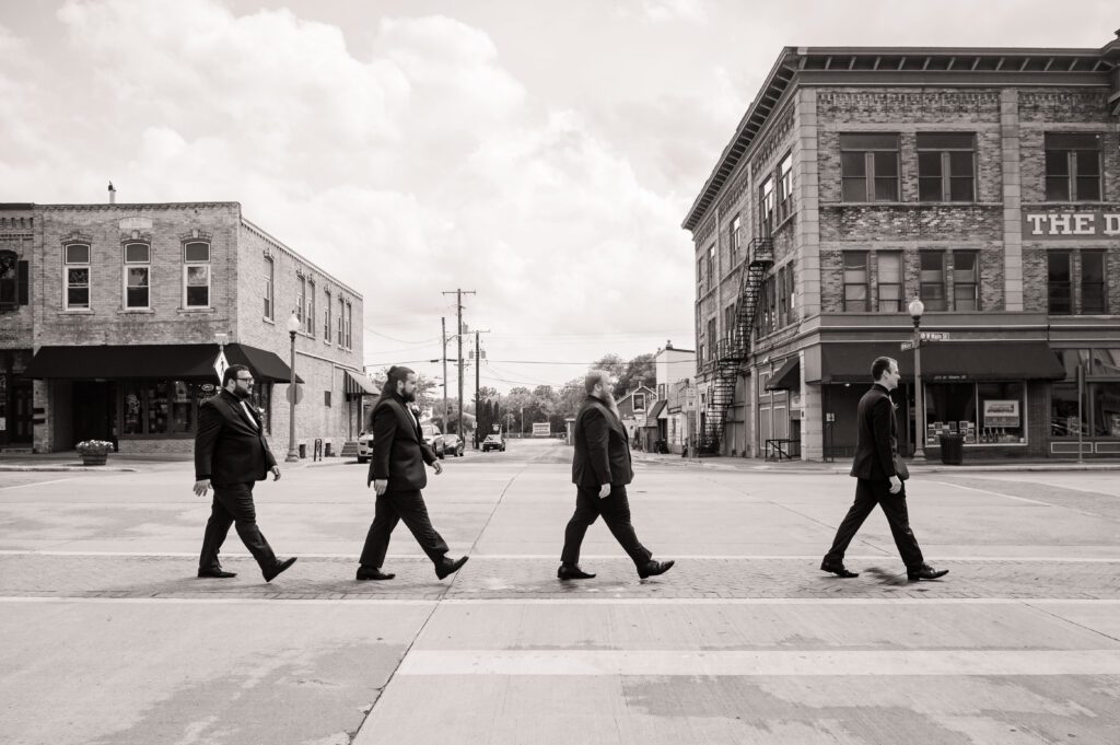 Groomsmen walking across the street in downtown Stoughton in a playful Abbey Road inspired portrait before Marissa and Jared’s Chorus Public House wedding.