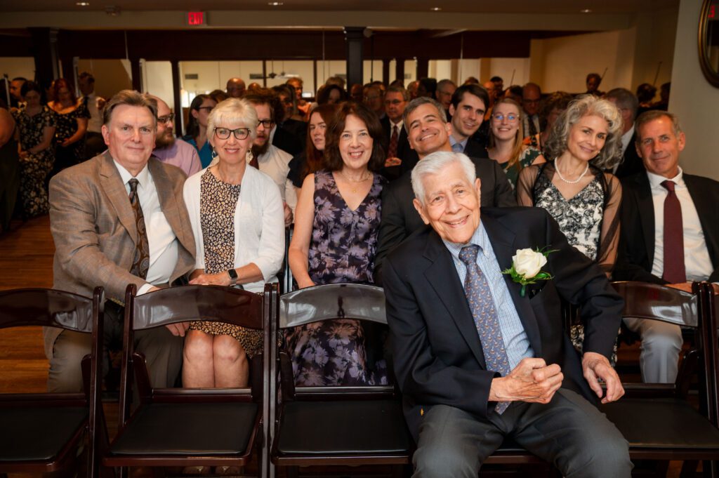Guests smiling and seated before Marissa and Jared’s ceremony at Chorus Public House, Stoughton WI, captured by Danielle Lund Photography.