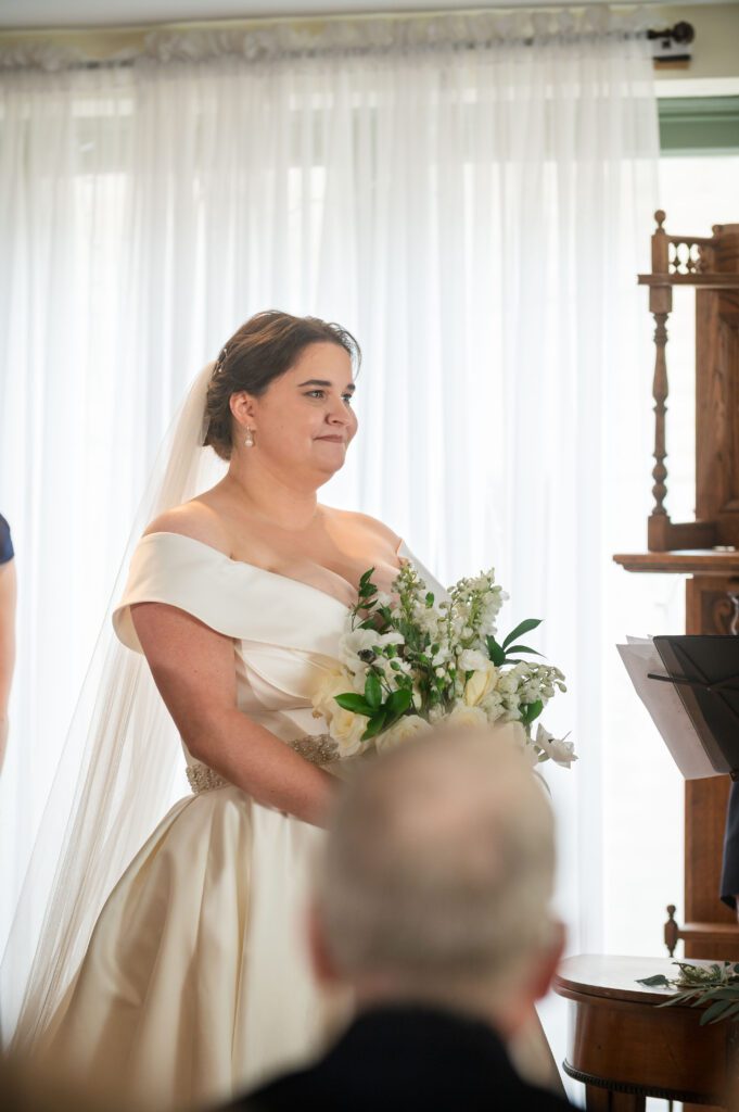 Bride Marissa holding a bouquet of white and green florals, looking emotional during the wedding ceremony at Chorus Public House.