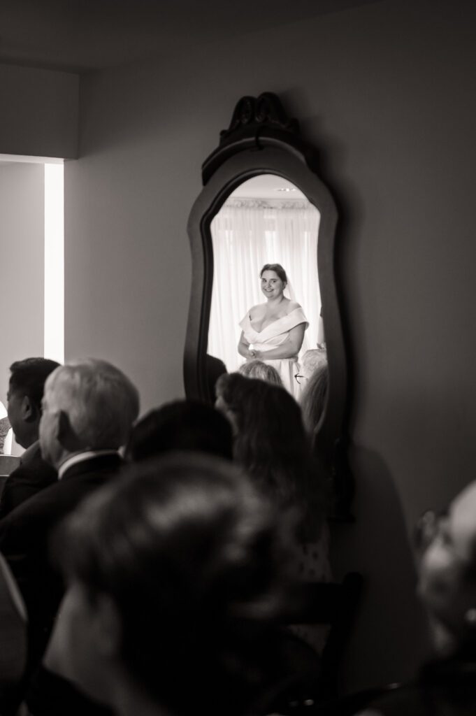 Bride Marissa reflected in a vintage mirror, smiling as she stands at the altar during the wedding ceremony at Chorus Public House.