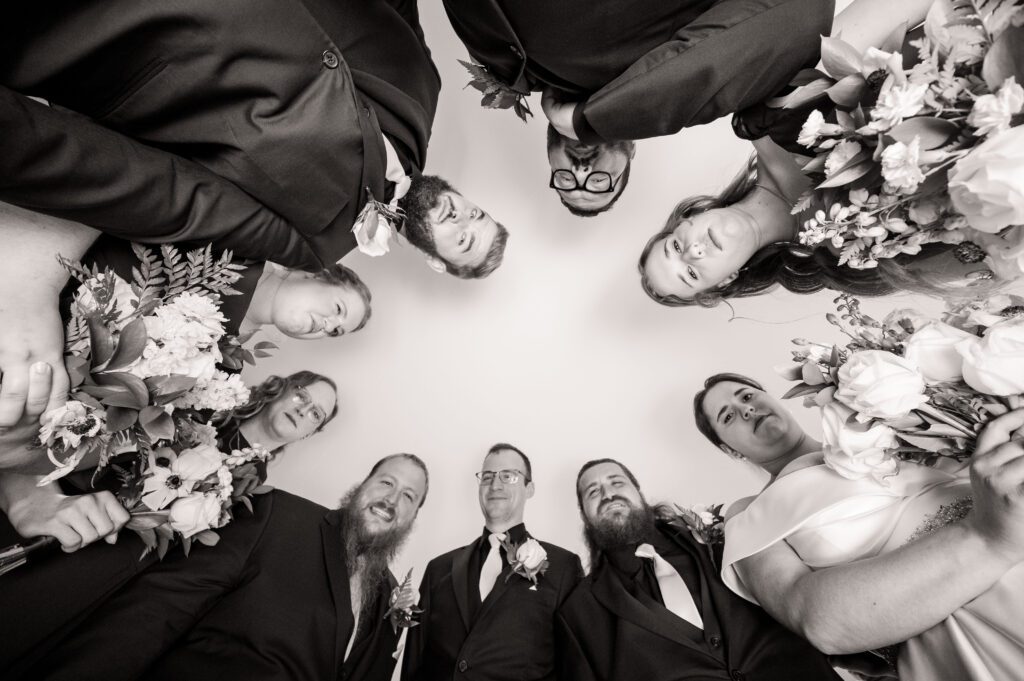 Creative bridal party portrait with bridesmaids and groomsmen circling Marissa and Jared, holding bouquets and looking down at the camera, Chorus Public House wedding.