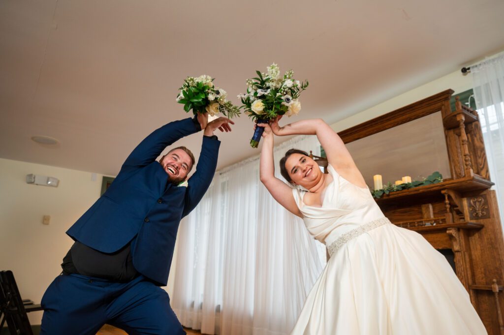 Fun wedding portrait of Marissa and Jared raising bouquets in a playful pose inside Chorus Public House on their wedding day.